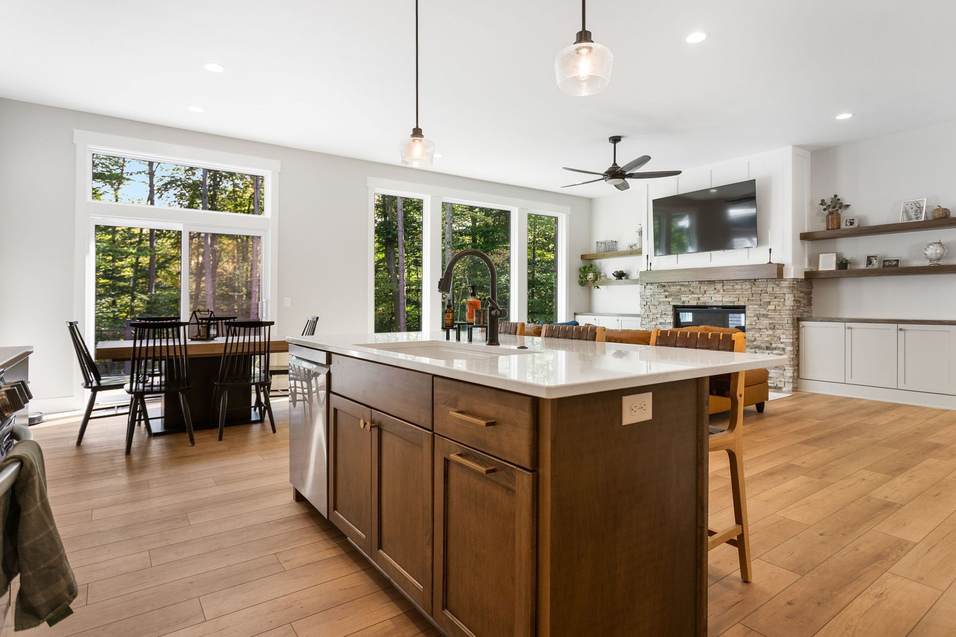 Open-plan kitchen and dining area with a wood island, light wood floors, and a stone fireplace in the living room.