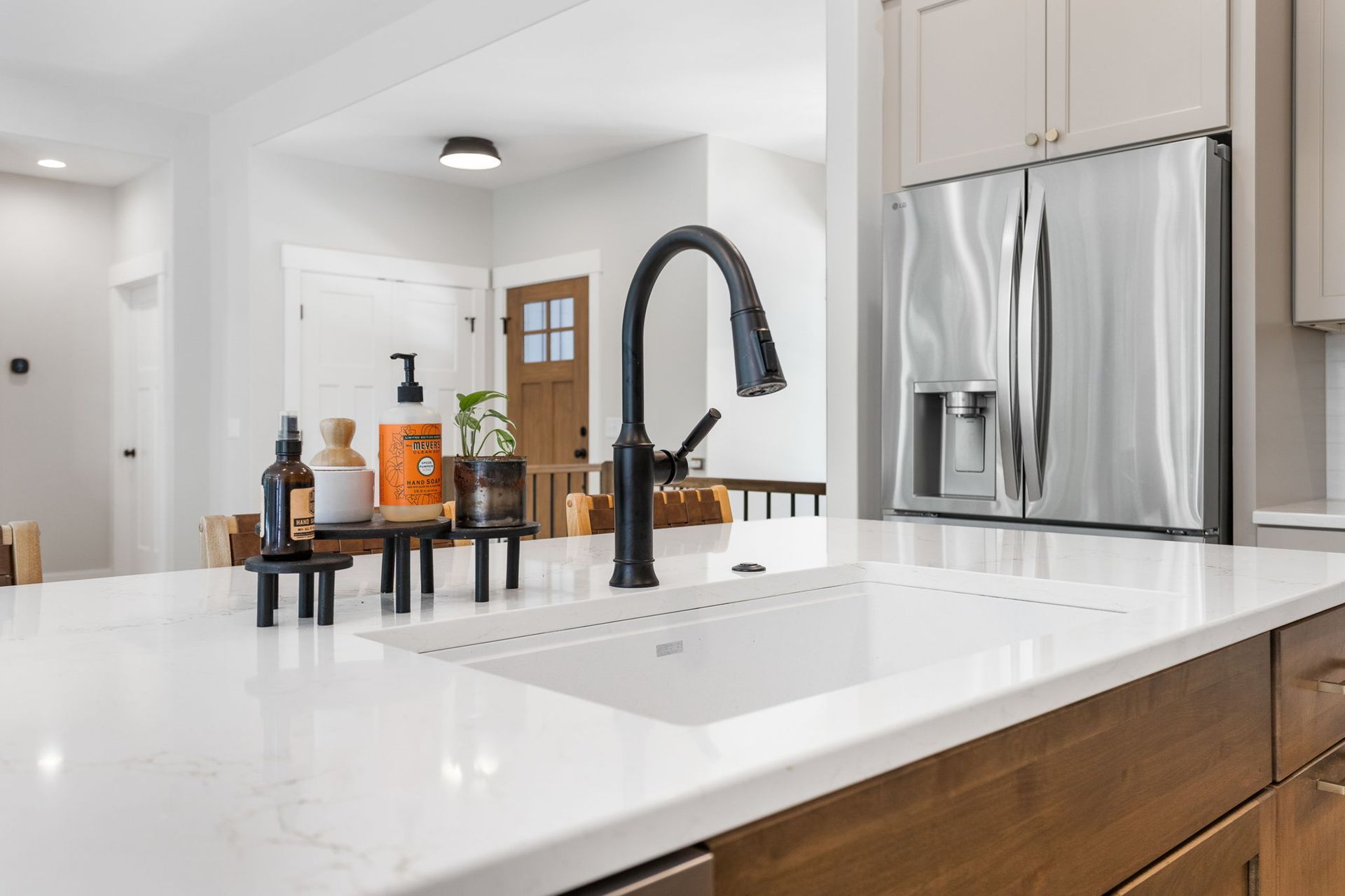 A white marble kitchen island with a black faucet, sink, and soap dispensers, with a refrigerator in the background.