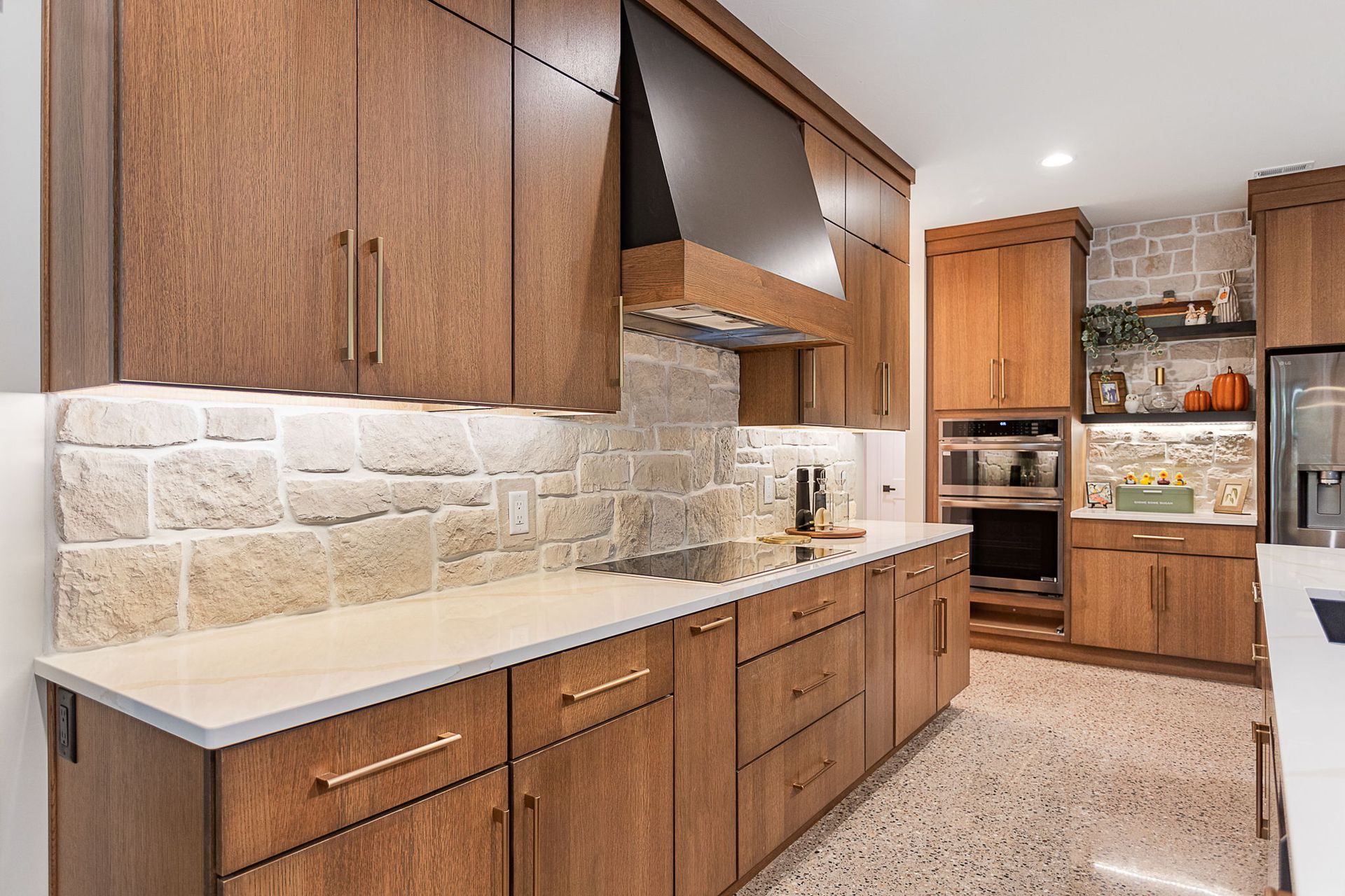 A modern kitchen featuring rich wood cabinets, a light stone backsplash, quartz countertops, and a stainless steel range.