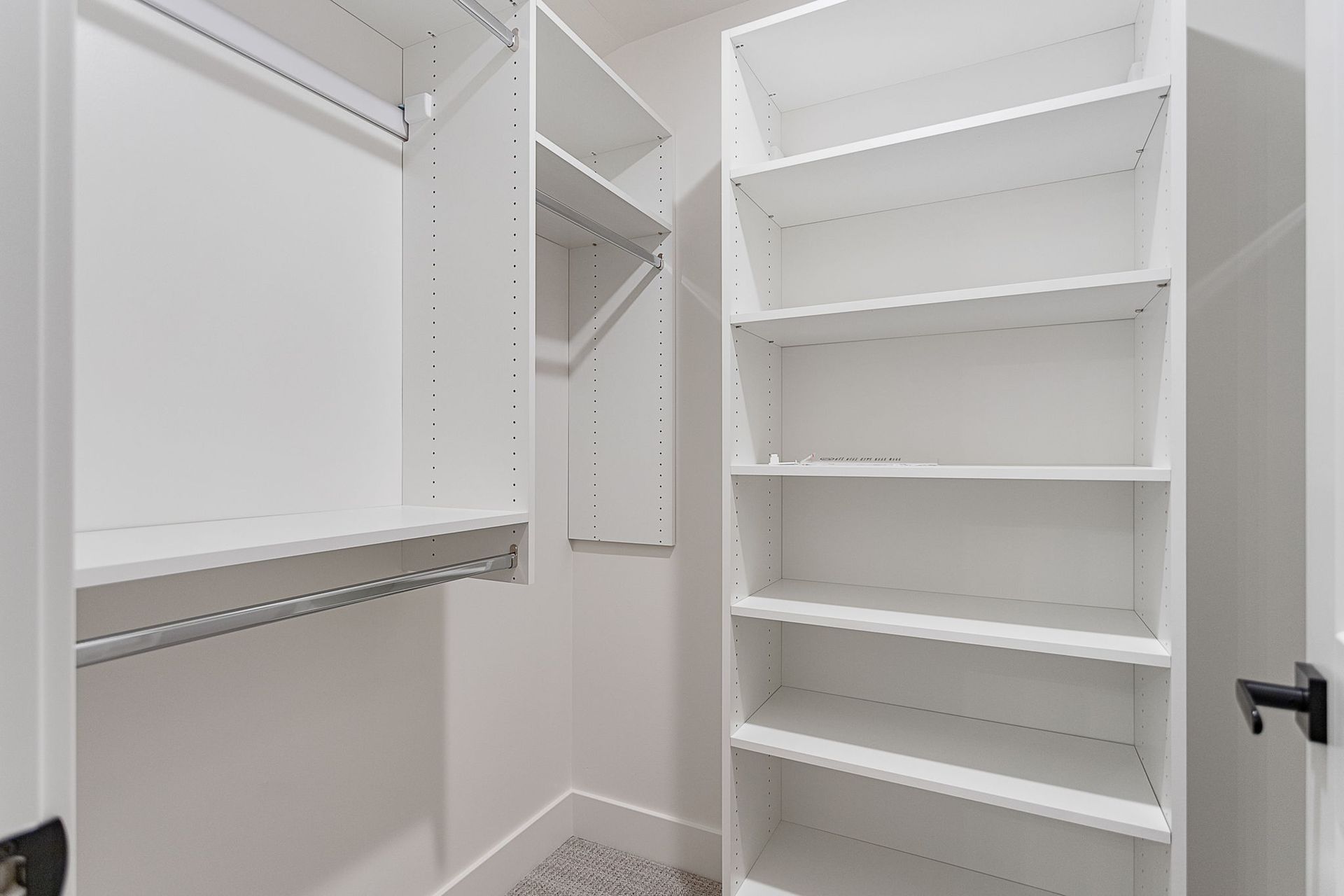 A walk-in closet featuring white wooden shelves and a hanging rod against neutral walls with light-colored carpeting.