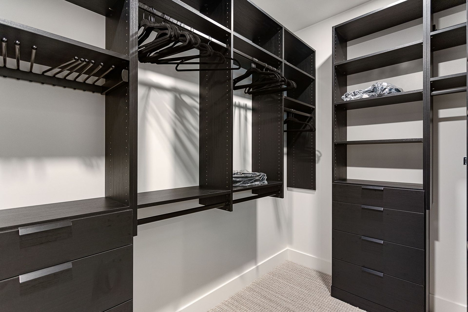 A walk-in closet featuring dark wood shelving, hanging racks, and built-in drawers against light-colored walls.