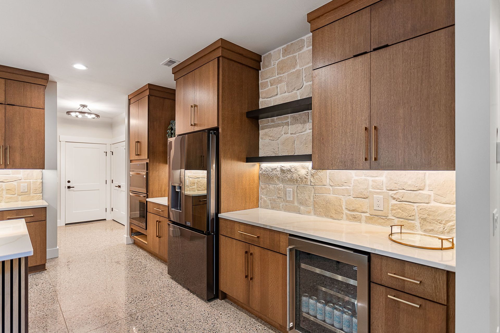 A modern kitchen featuring wooden cabinets, light stone backsplash, stainless steel appliances, and a wine cooler.