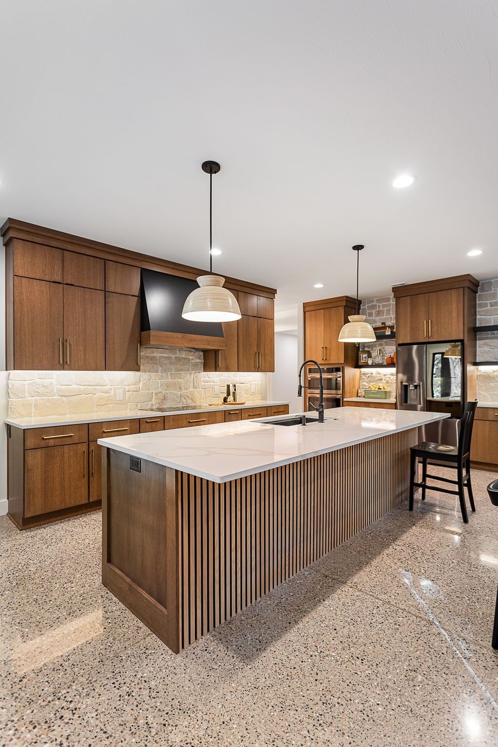 A modern kitchen with wood cabinets, white countertops, a slatted kitchen island, and speckled terrazzo flooring.
