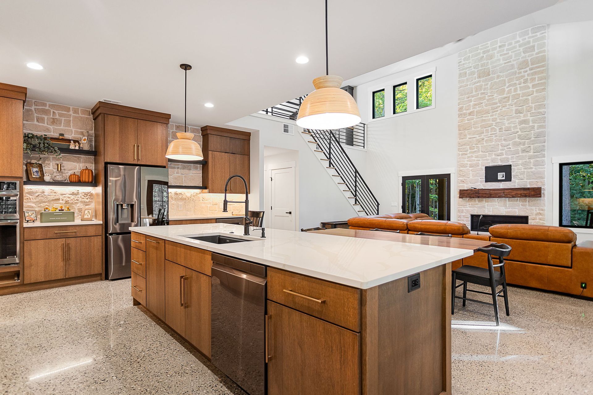 Modern kitchen with a large island, wood cabinets, stone fireplace, and open floor plan with high ceilings.