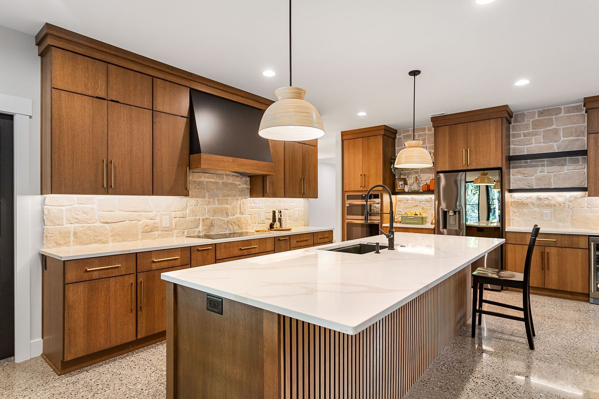 Modern kitchen with wood cabinets, light stone backsplash, a large white island, and hanging pendant lights.
