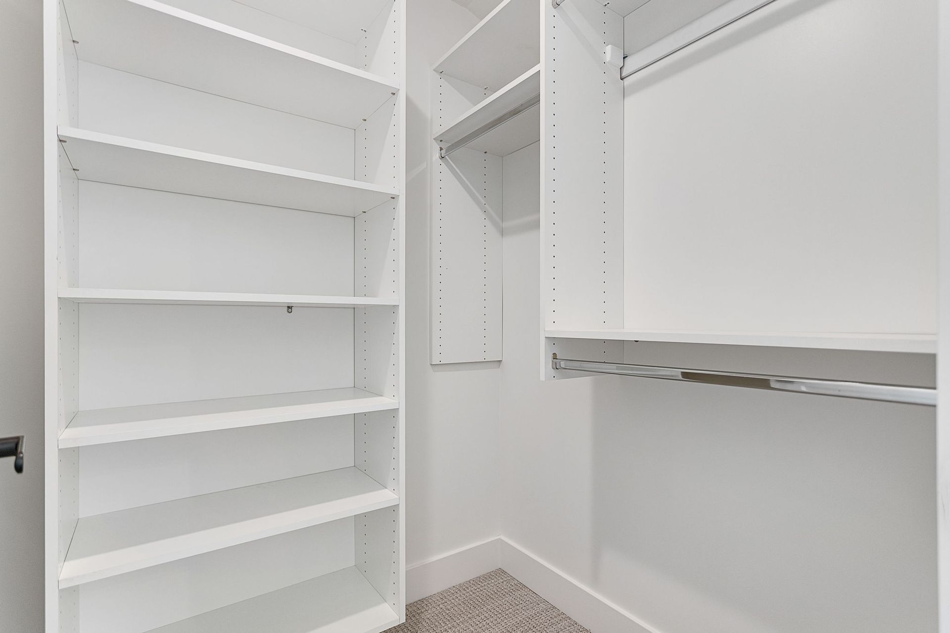 A walk-in closet featuring white wooden shelving units and a hanging rod against neutral walls with carpeted flooring.