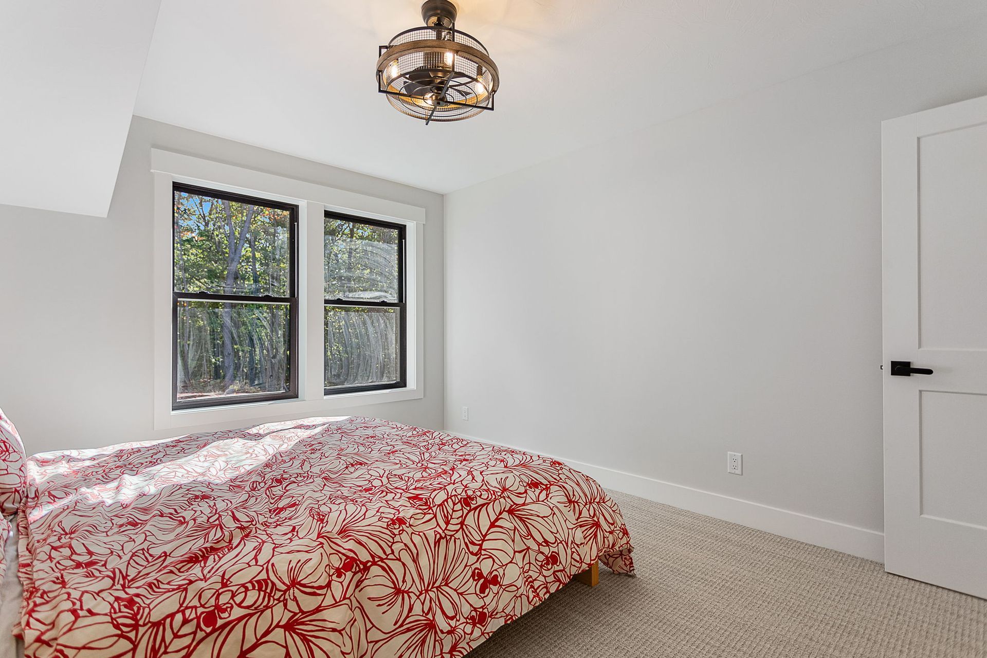A bedroom featuring a bed with a red and white patterned comforter, two windows, neutral walls, and a ceiling fan.