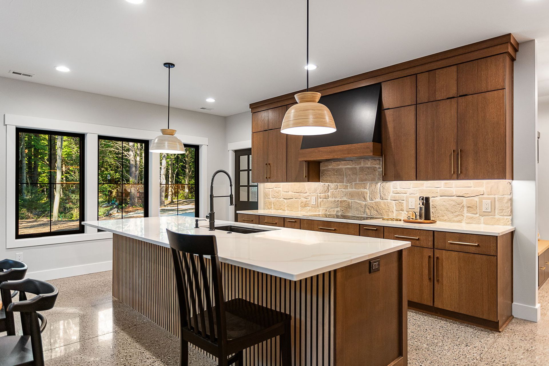 A kitchen with wood cabinets, a stone backsplash, a large white kitchen island with seating, and black window frames.