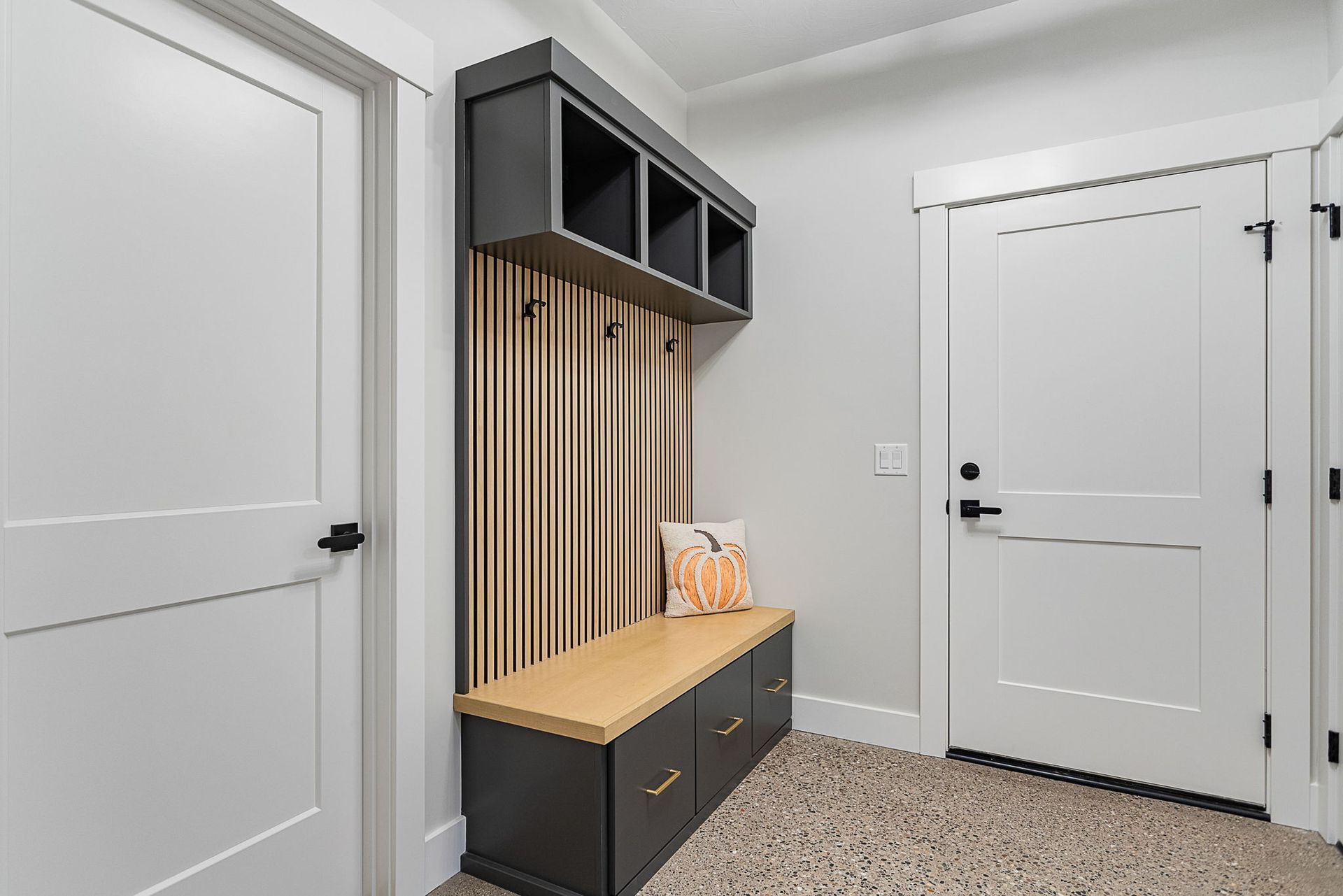 A mudroom entryway featuring a dark built-in bench with storage, wooden slat wall paneling, and two white interior doors.