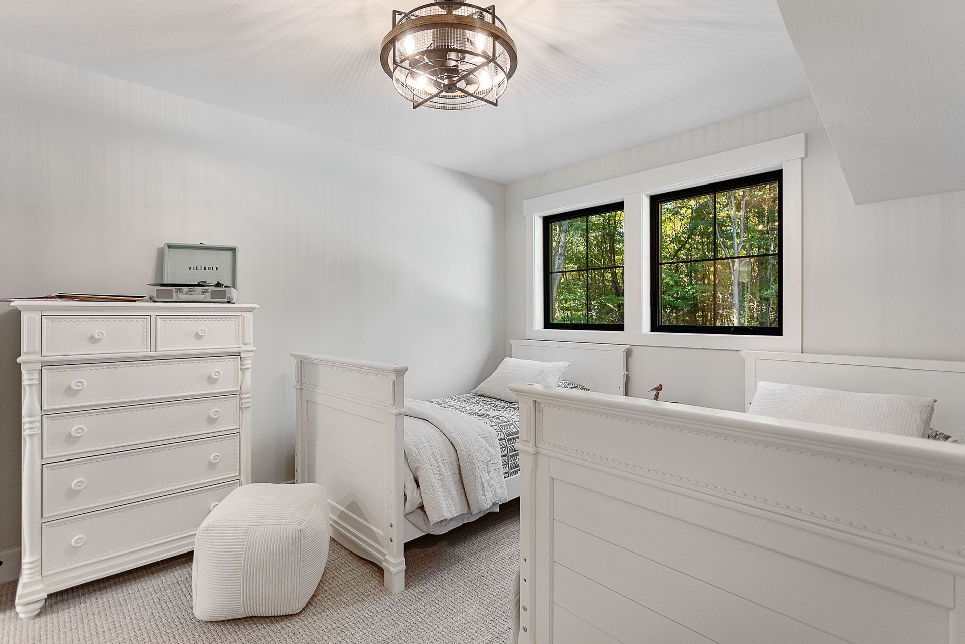 A white bedroom featuring two twin beds, a matching dresser, a small stool, and a round metal light fixture.