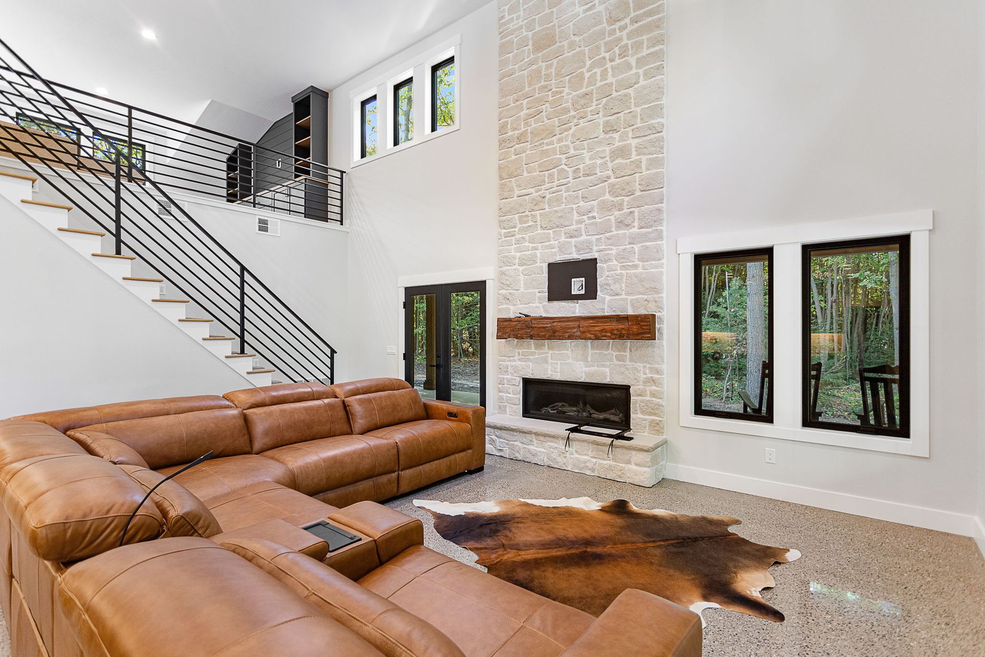 A spacious living room with a large tan sectional sofa, a stone fireplace, high ceilings, and a staircase.