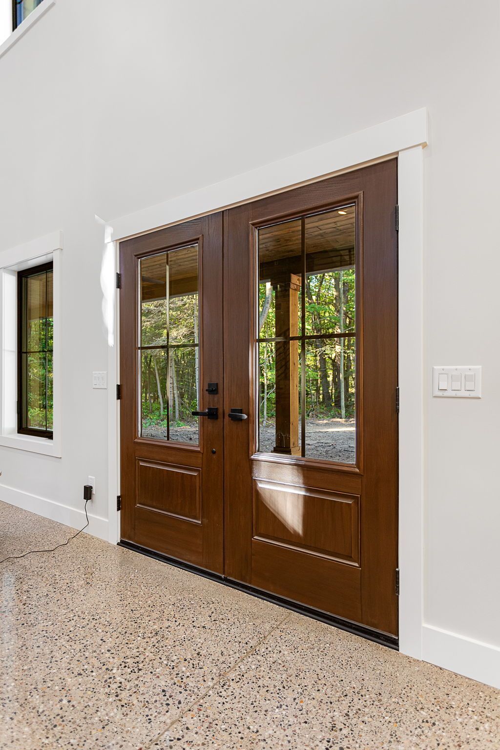 Double dark wood French doors with glass panes, set in a white wall above a speckled light-colored floor.