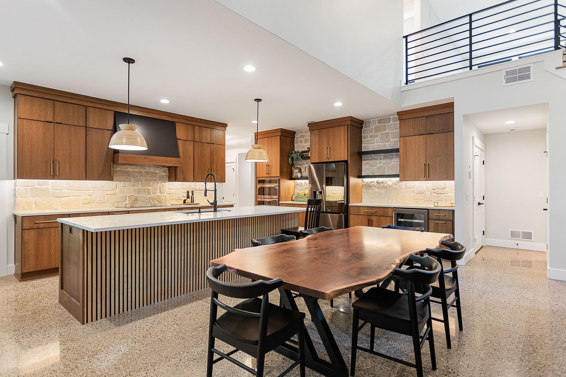 Modern kitchen with wood cabinets, a large slatted island, and a live-edge wood dining table with black chairs.