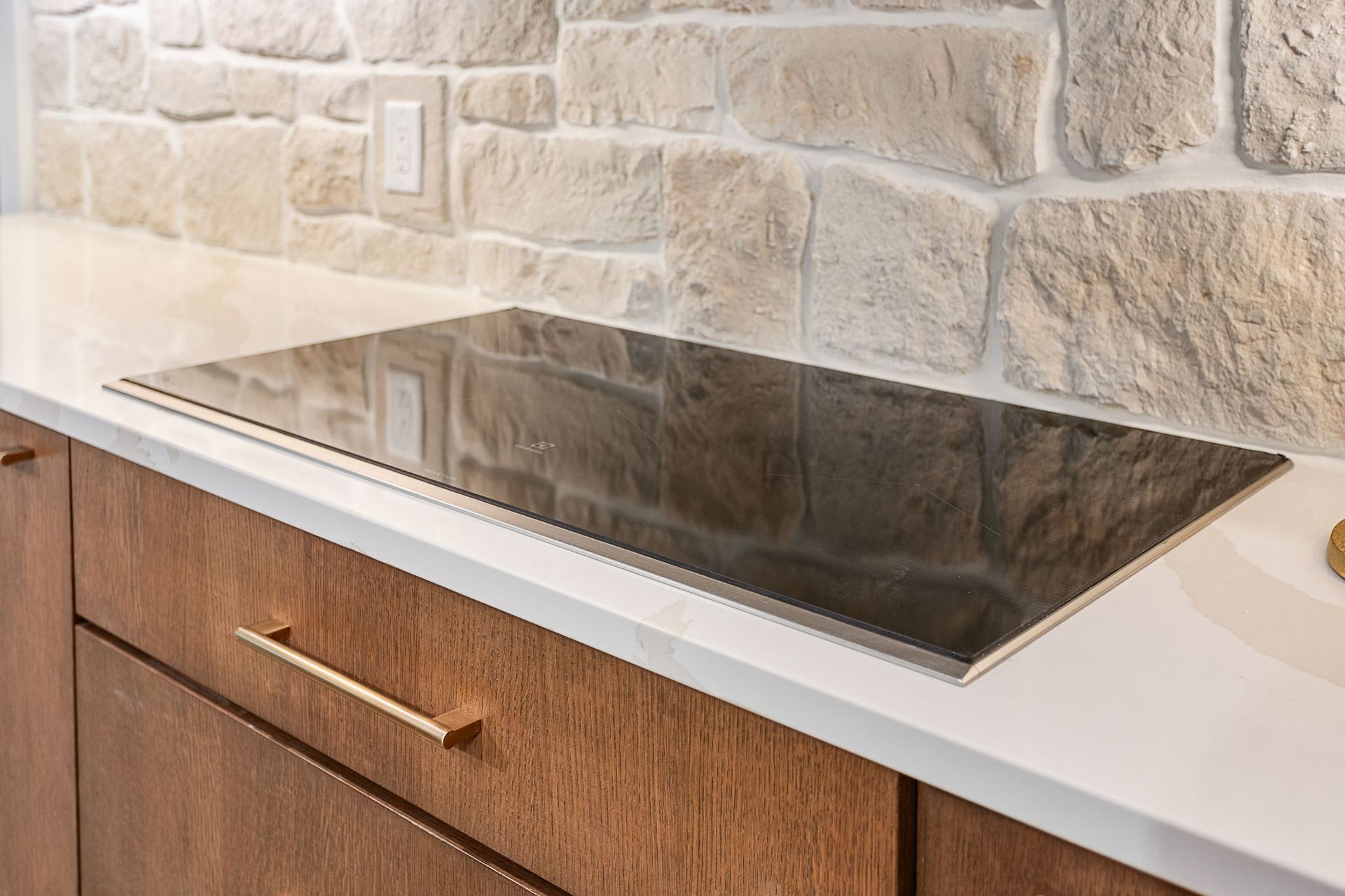 A sleek black induction cooktop set into a white countertop in front of a light-colored stacked stone backsplash.