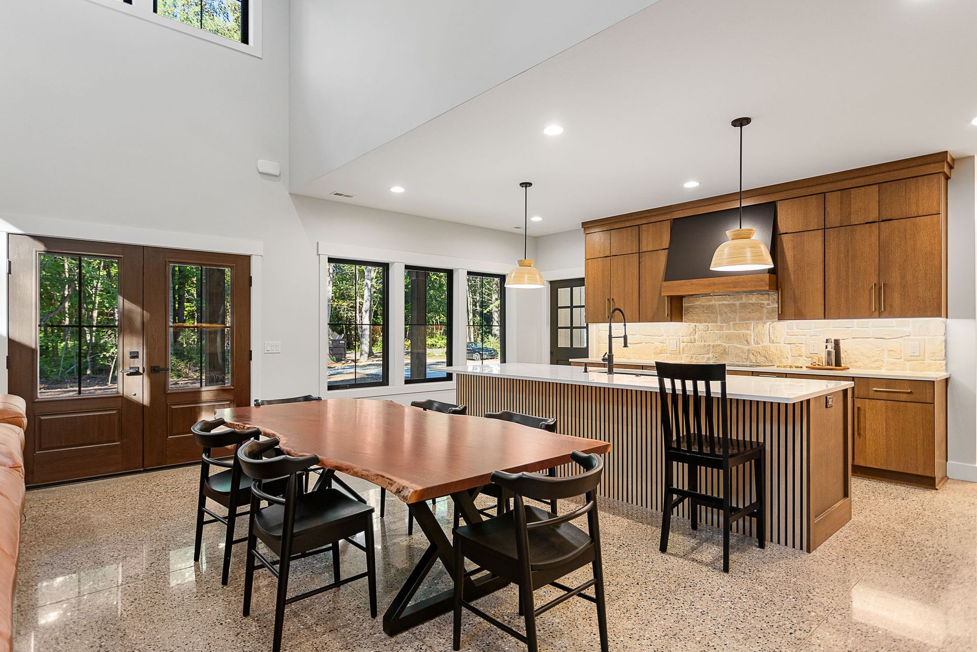Modern kitchen and dining area with wood cabinets, stone-flecked floors, a long wooden table, and high ceilings.