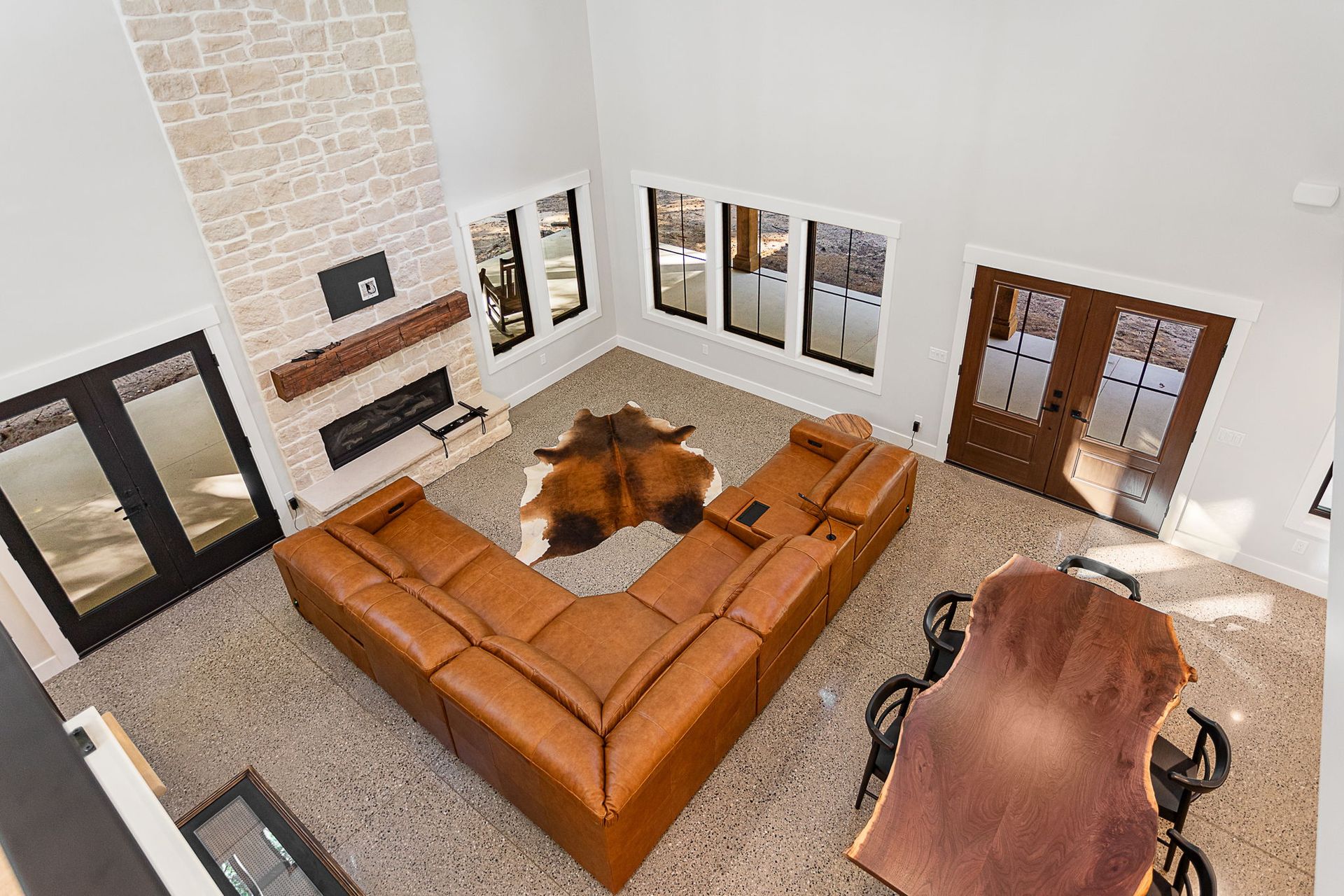 High-angle view of a modern living room featuring a tan sectional, cowhide rug, stone fireplace, and a dining table.