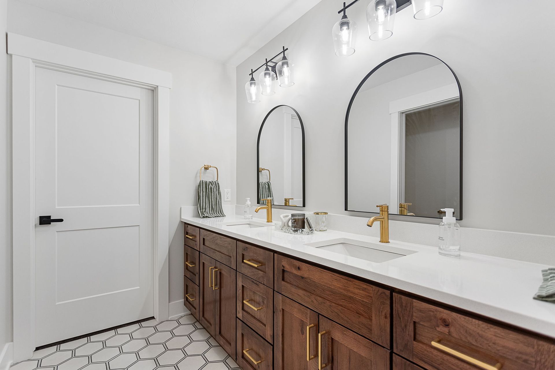 A double-sink bathroom vanity with wood cabinets, gold hardware, arched mirrors, and white countertops.