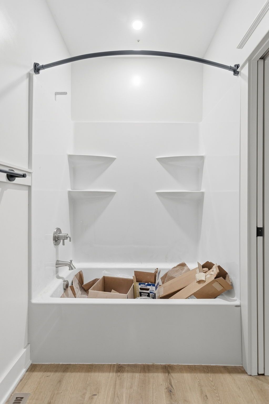 Bathroom under renovation with white tub, built-in shelves, and cardboard debris on wood floor