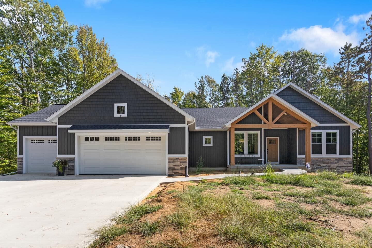 A modern single-story house with dark grey horizontal siding, a two-car garage, and a timber-framed front porch.