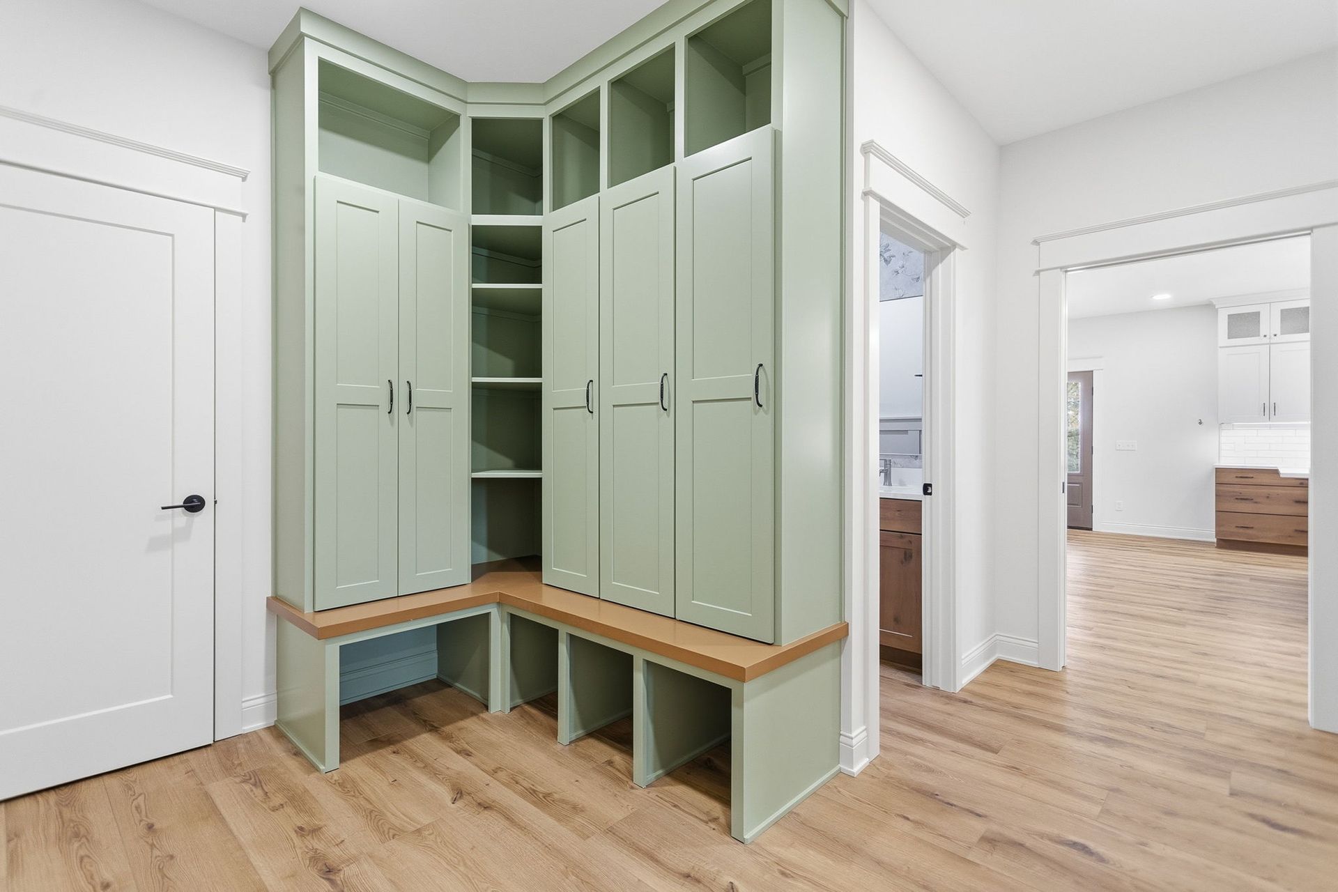 Built-in mint-green mudroom cabinets with bench seating in a bright hallway