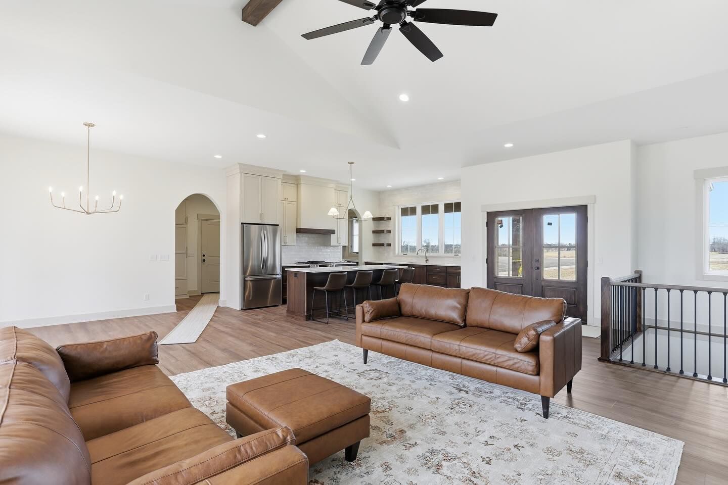 Open-concept living room and kitchen featuring brown leather sofas, a patterned rug, and a vaulted ceiling with a fan.