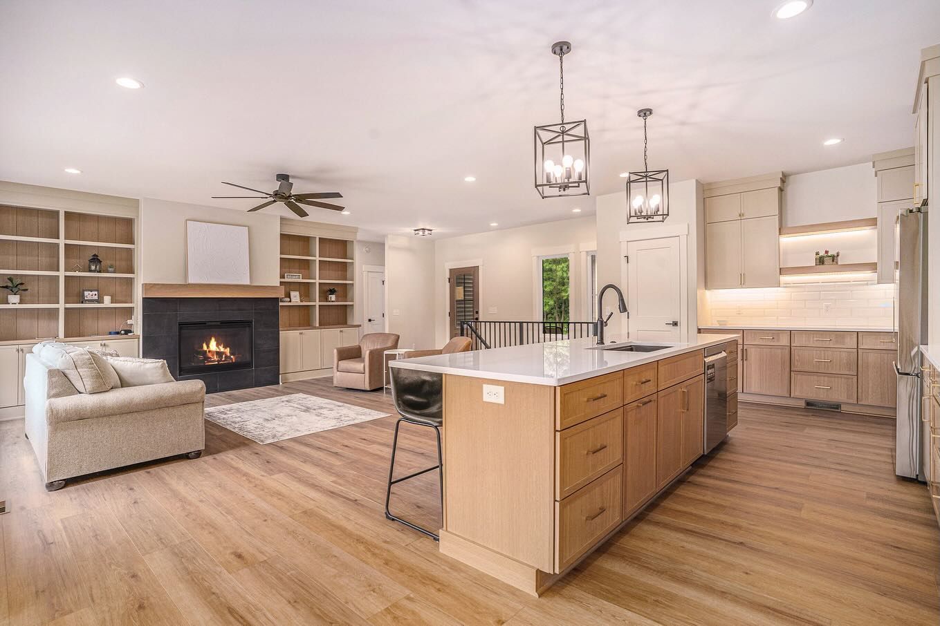 Open-concept living room and kitchen with a fireplace, beige sofa, wooden cabinets, and an island with bar seating.