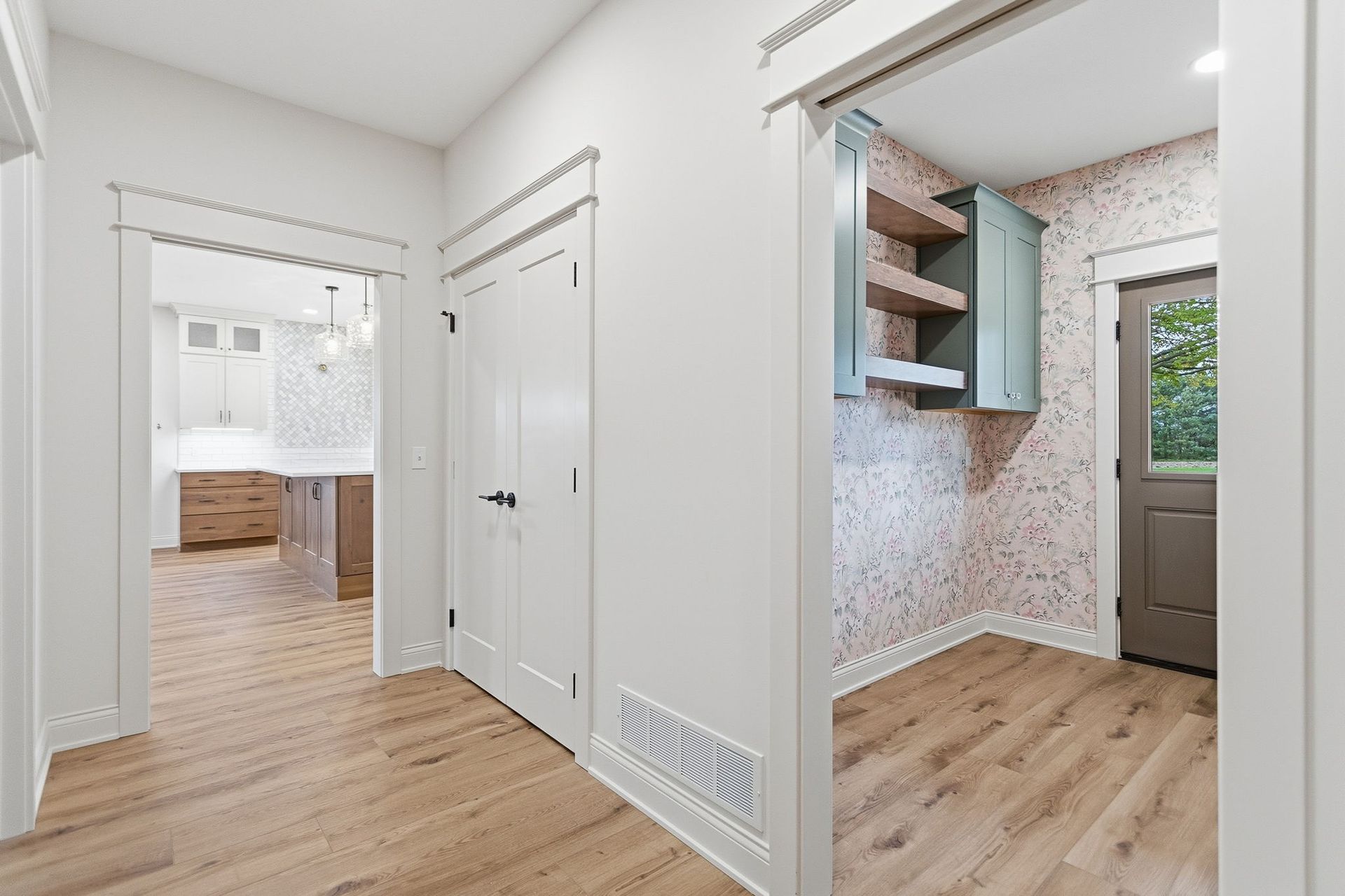 A bright, empty room with light wood floors, a vaulted ceiling, a ceiling fan, and white board-and-batten wall trim.
