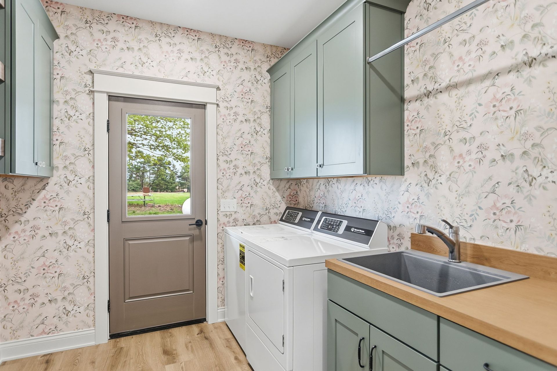Laundry room with cabinets, sink, washer, and a back door opening to greenery.