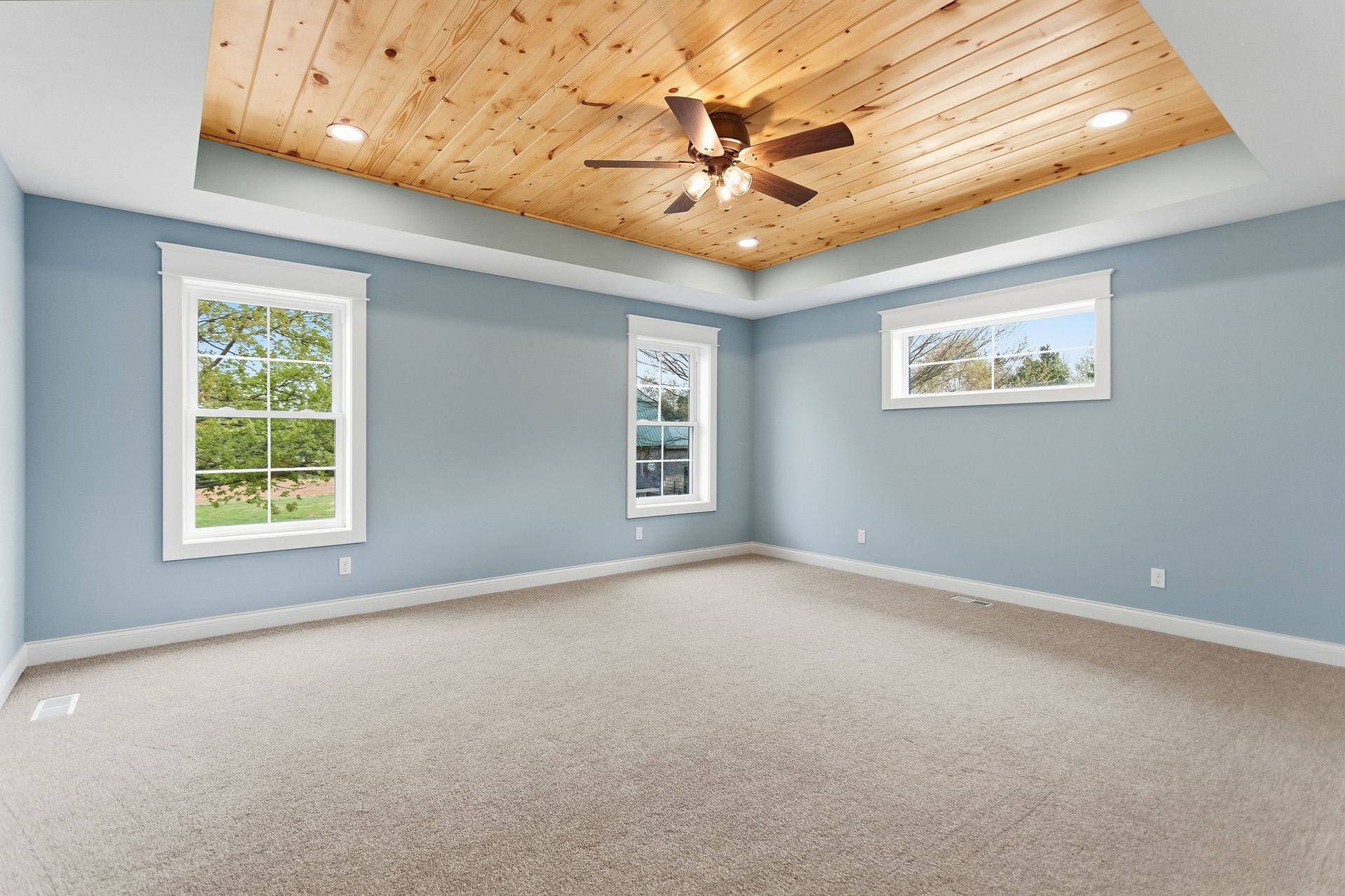 Empty bedroom with light blue walls, carpeted floor, and a wood-paneled ceiling with a ceiling fan