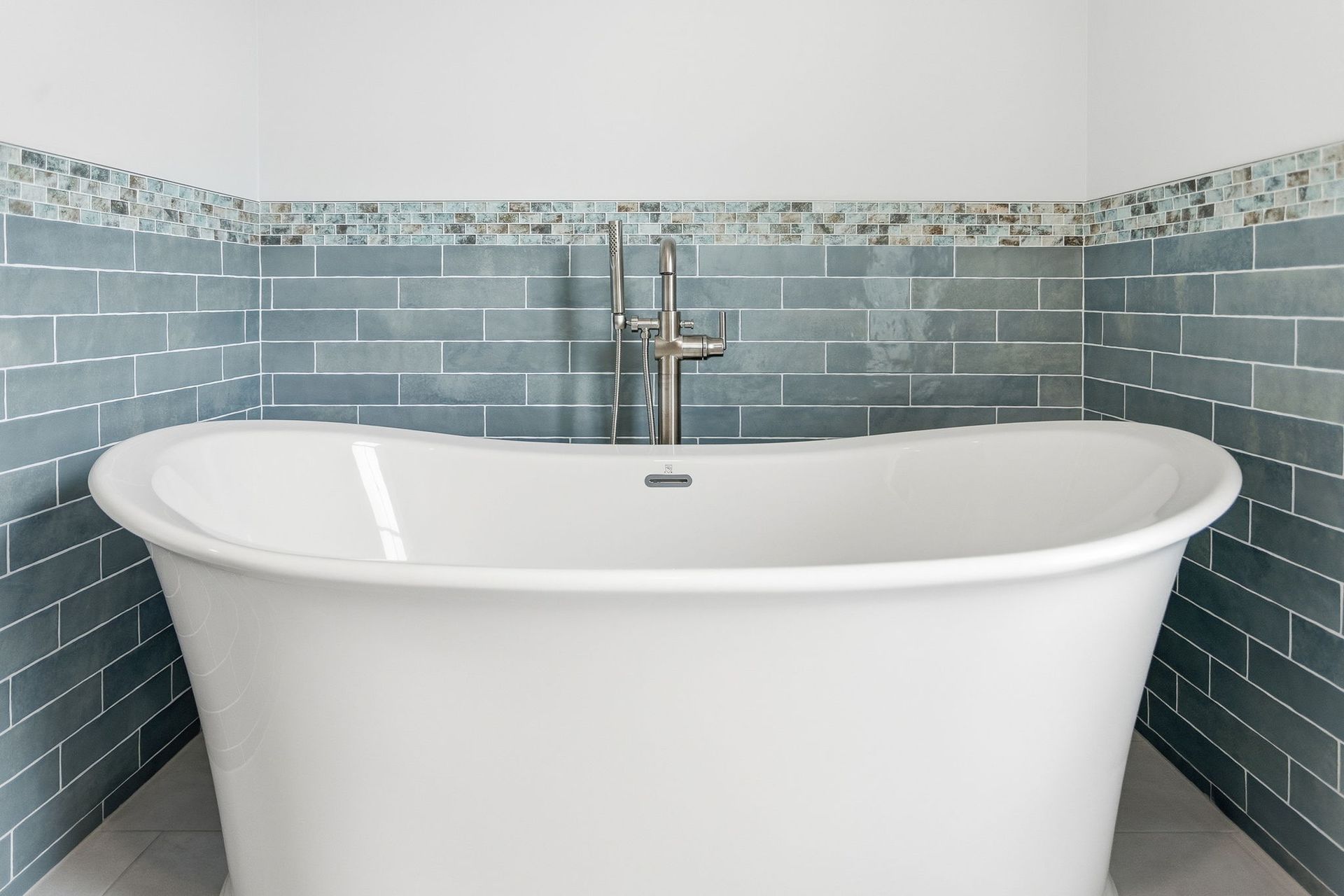 Freestanding white bathtub with chrome faucet against blue tile walls in a modern bathroom