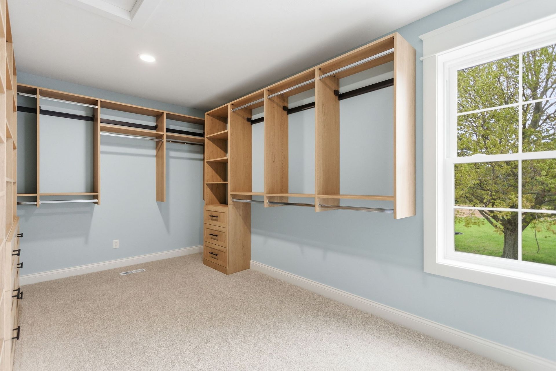 Walk-in closet with wood shelving, hanging rods, and a window overlooking a green yard.