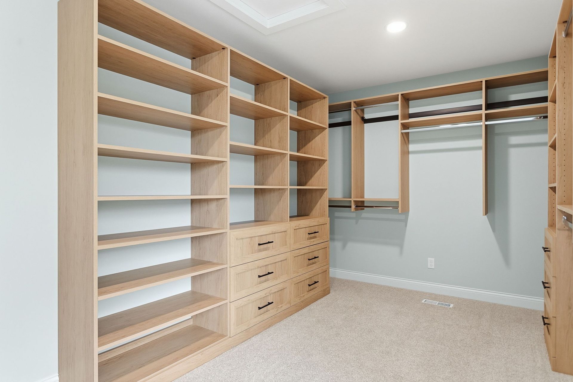 Walk-in closet with light wood shelves and drawers, hanging rods, and beige carpet.