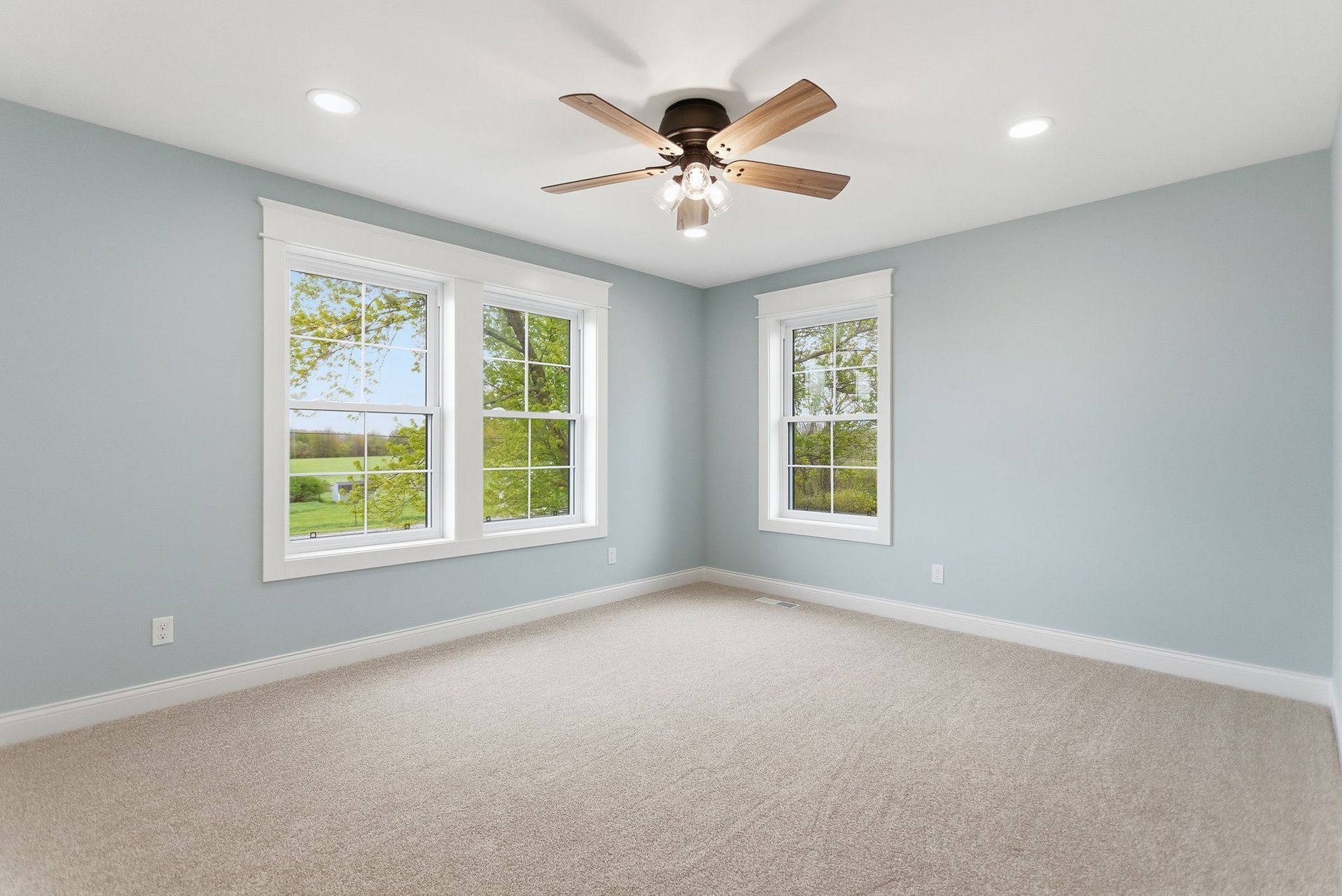 Empty light gray bedroom with carpet, two windows, and a ceiling fan with lights.