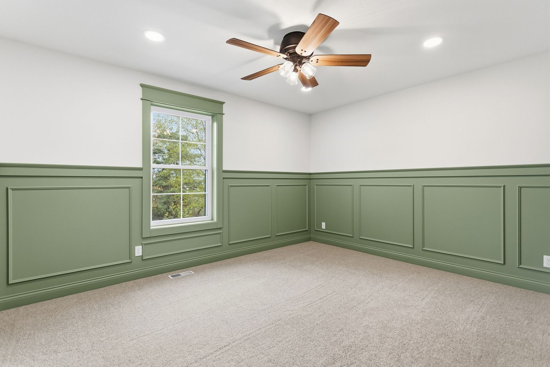 Empty room with sage green wainscoting, white walls, a window, carpet, and a ceiling fan.