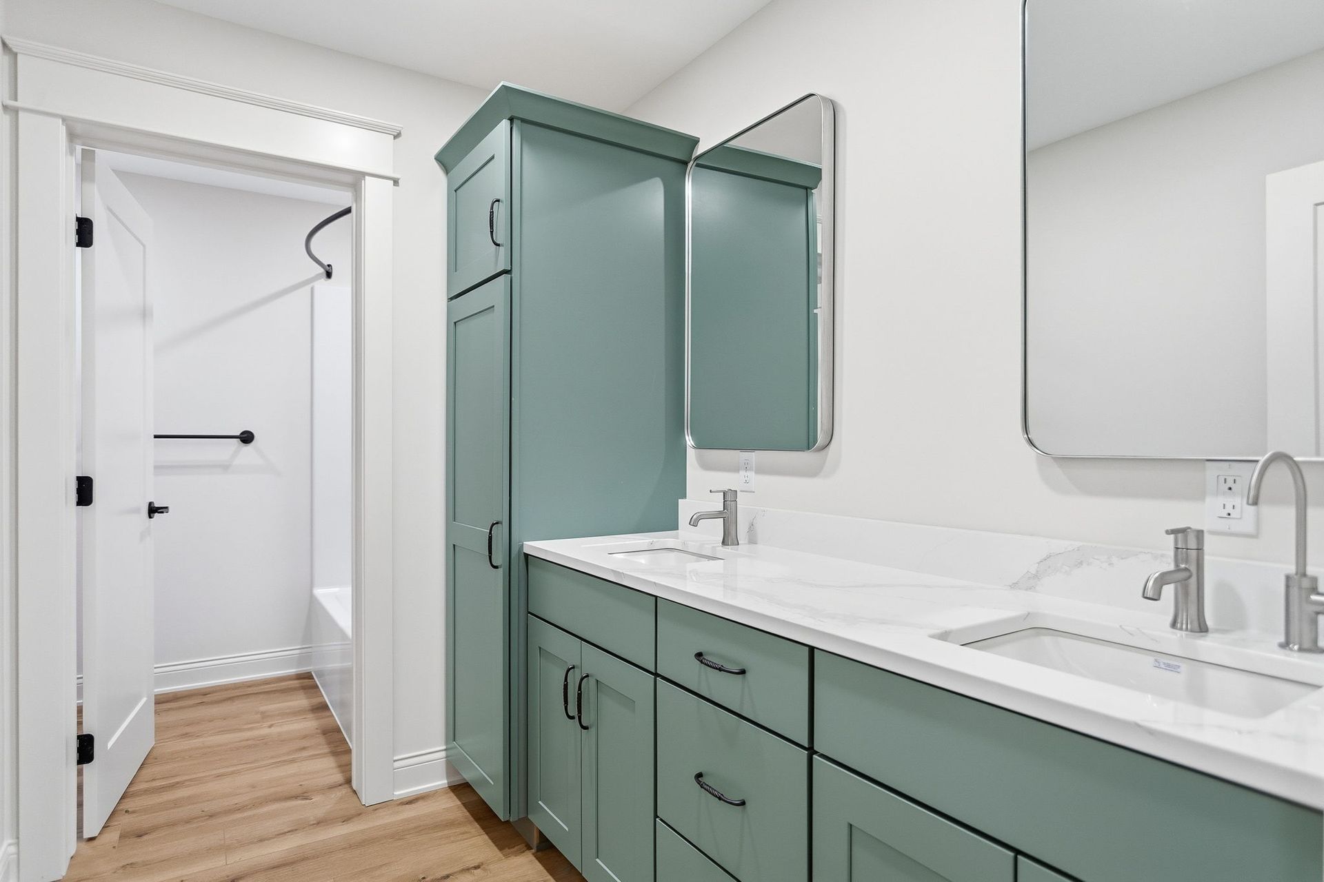 Modern bathroom with green vanity, double sinks, large mirror, and walk-in shower in the background