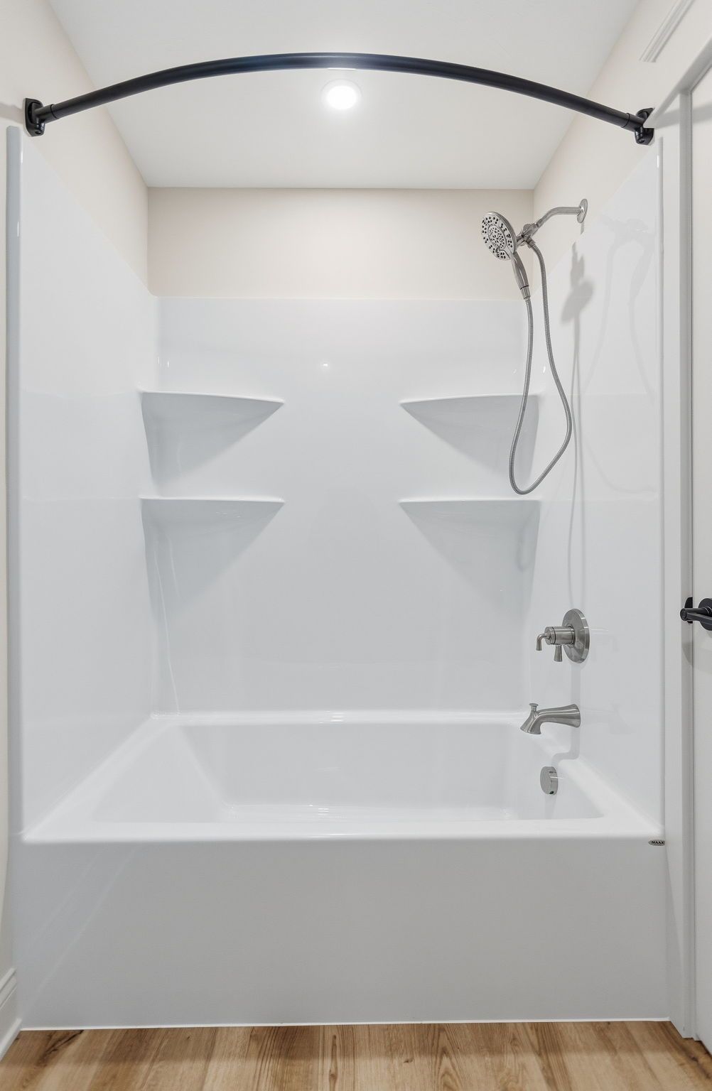 White walk-in shower with built-in shelves, handheld showerhead, and curved black grab bar.