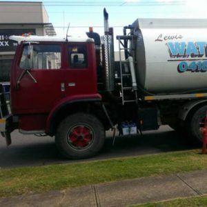 A red and white water tanker truck parked on the side of a street.