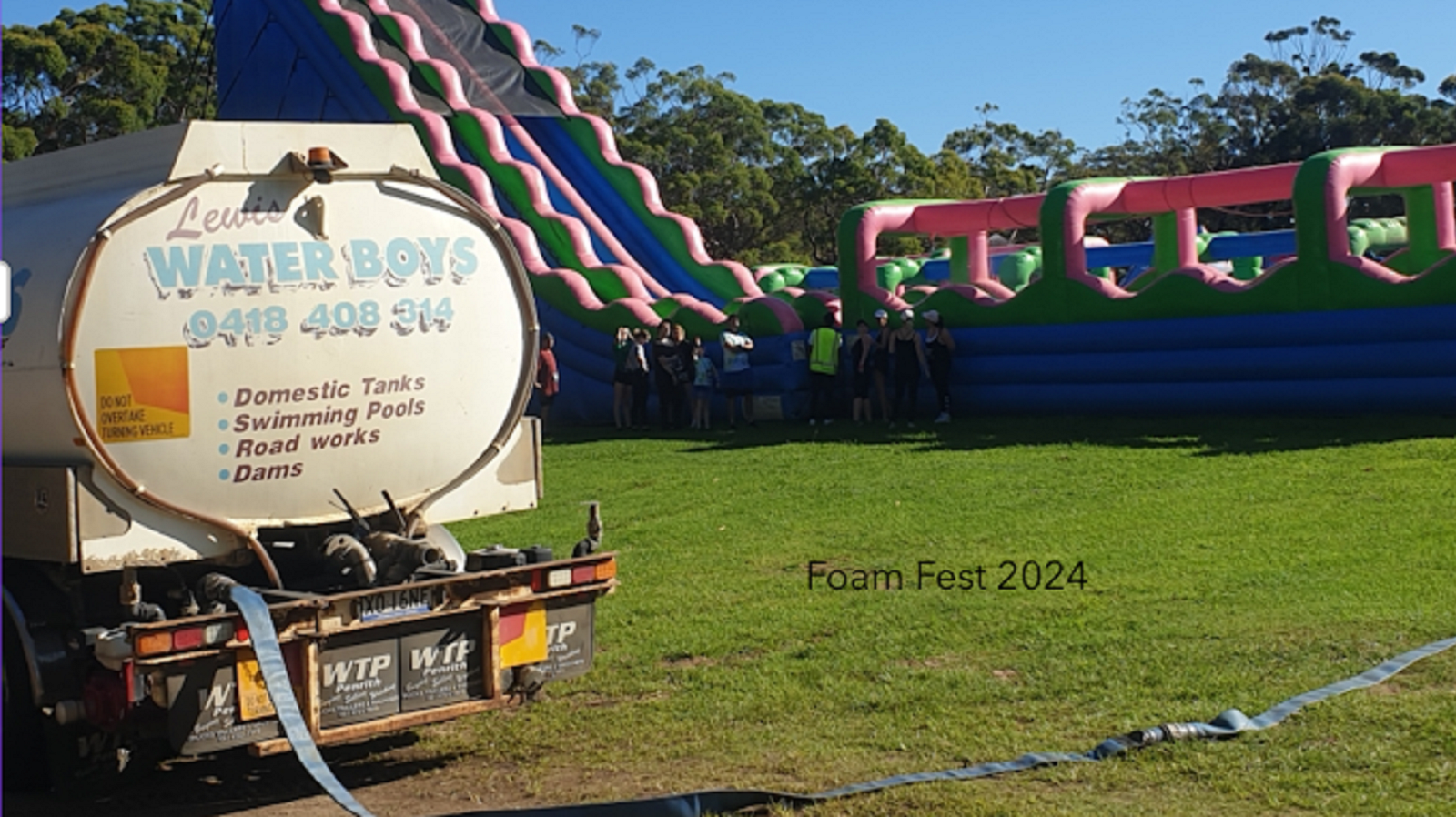 A water truck parked in a grassy field next to a large, colorful inflatable obstacle course and slide at Extern Fest 2024.