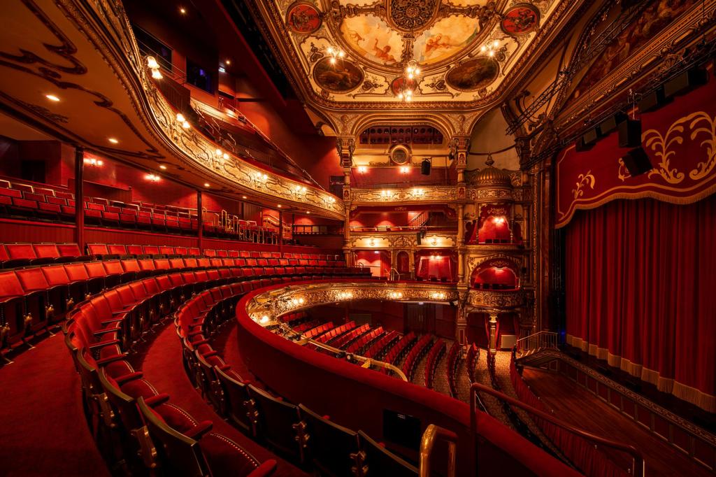 A large empty theatre with red seats and a red curtain.