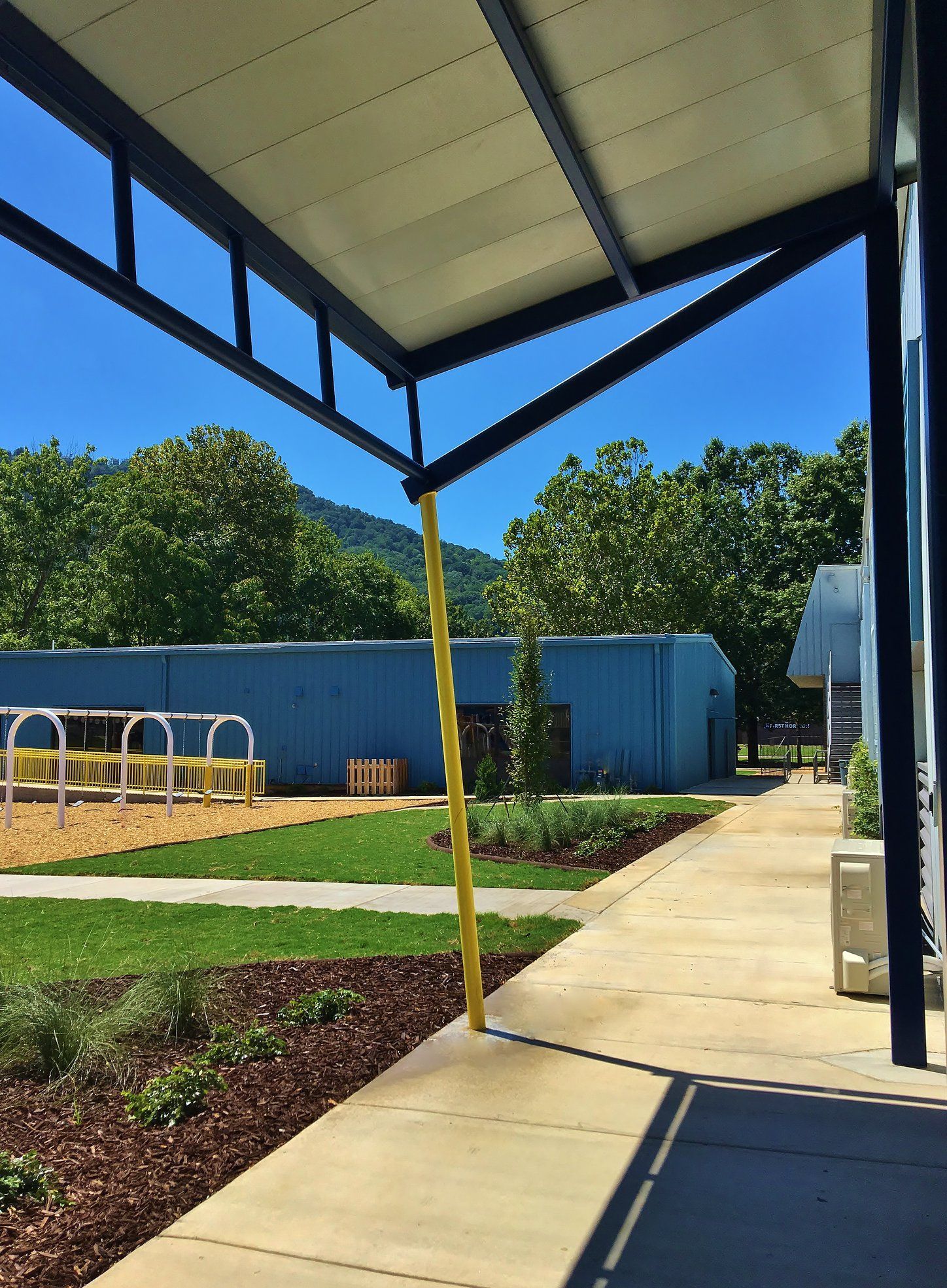 A covered walkway leading to a playground with a blue building in the background.