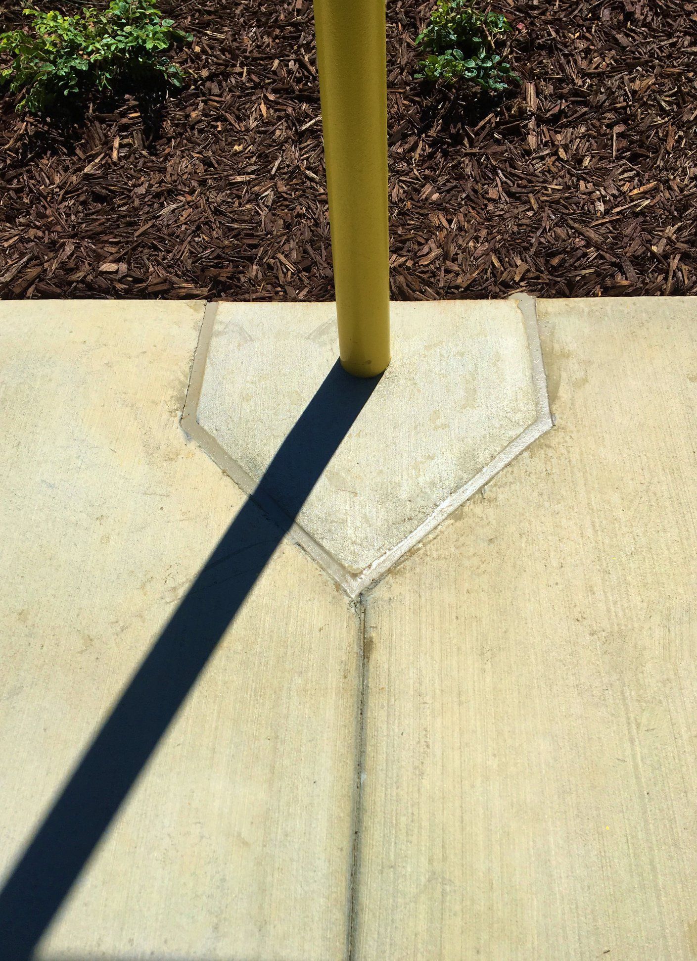 A shadow of a pole is cast on a concrete surface