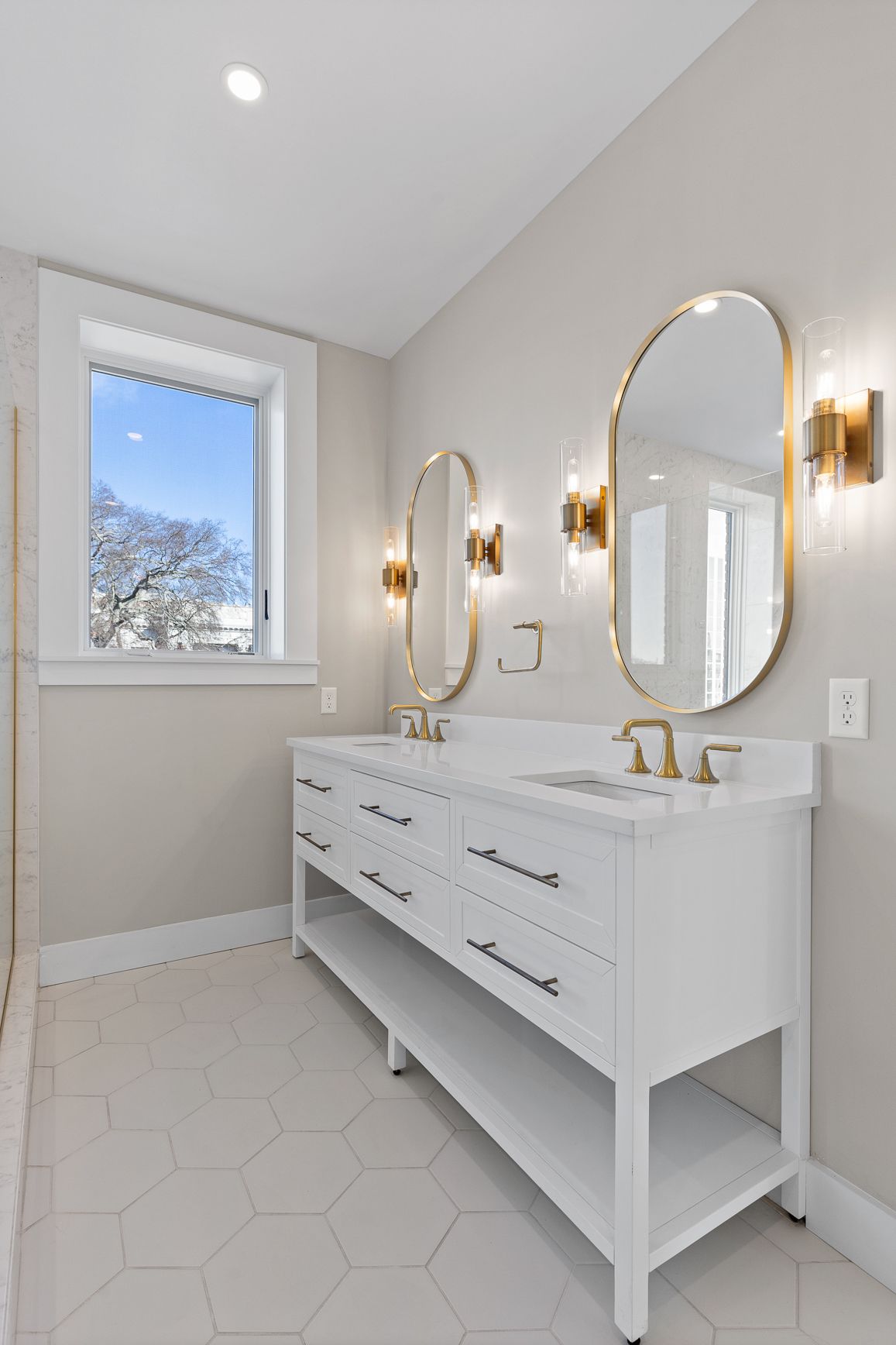 A bathroom with two sinks , two mirrors and a window.