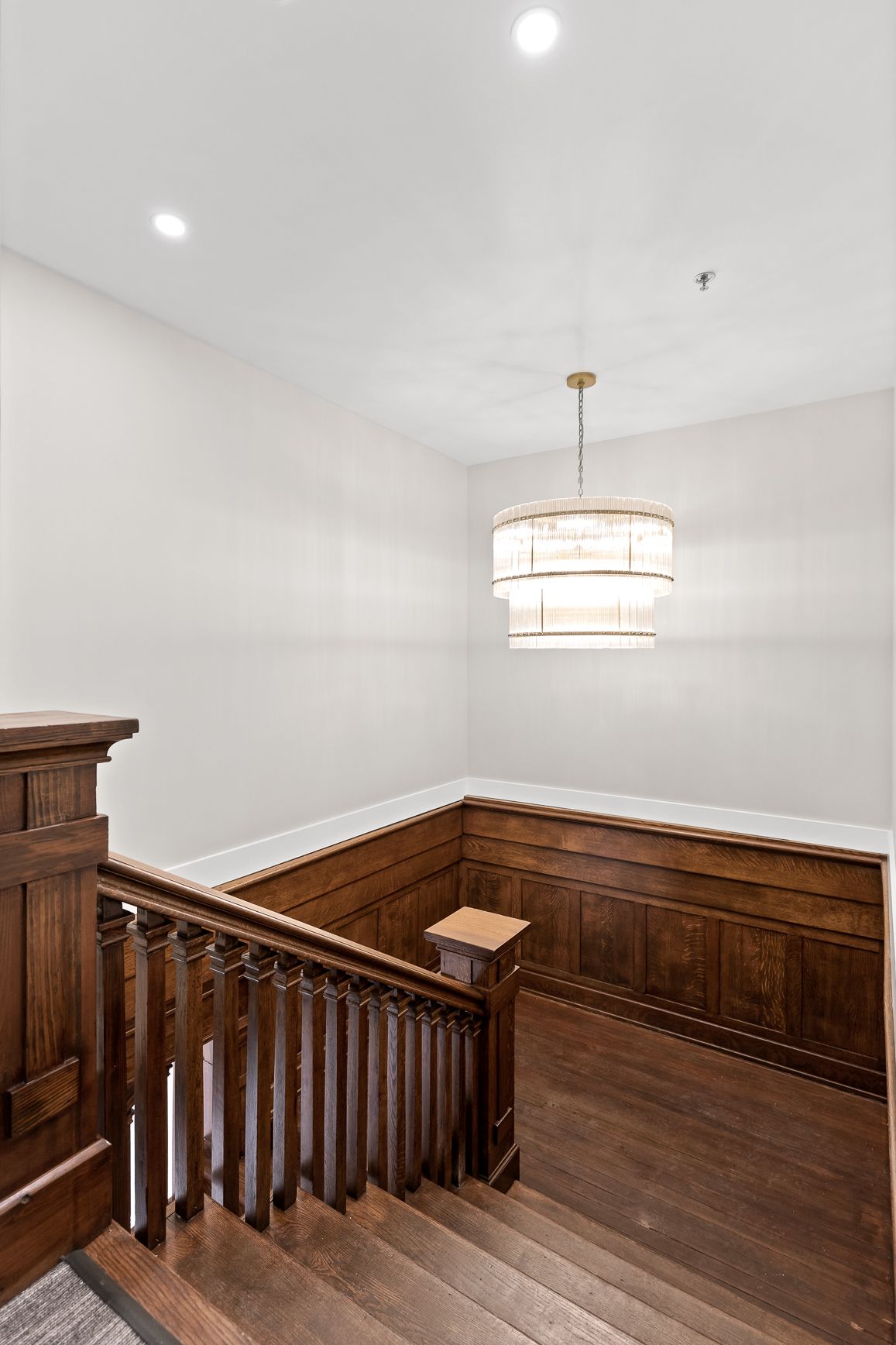 A staircase with a wooden railing and a chandelier hanging from the ceiling.