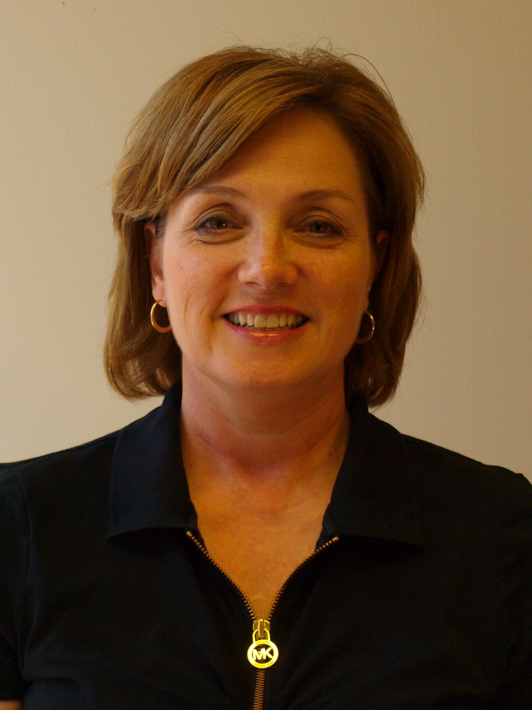 A woman wearing a black shirt with a gold zipper is smiling