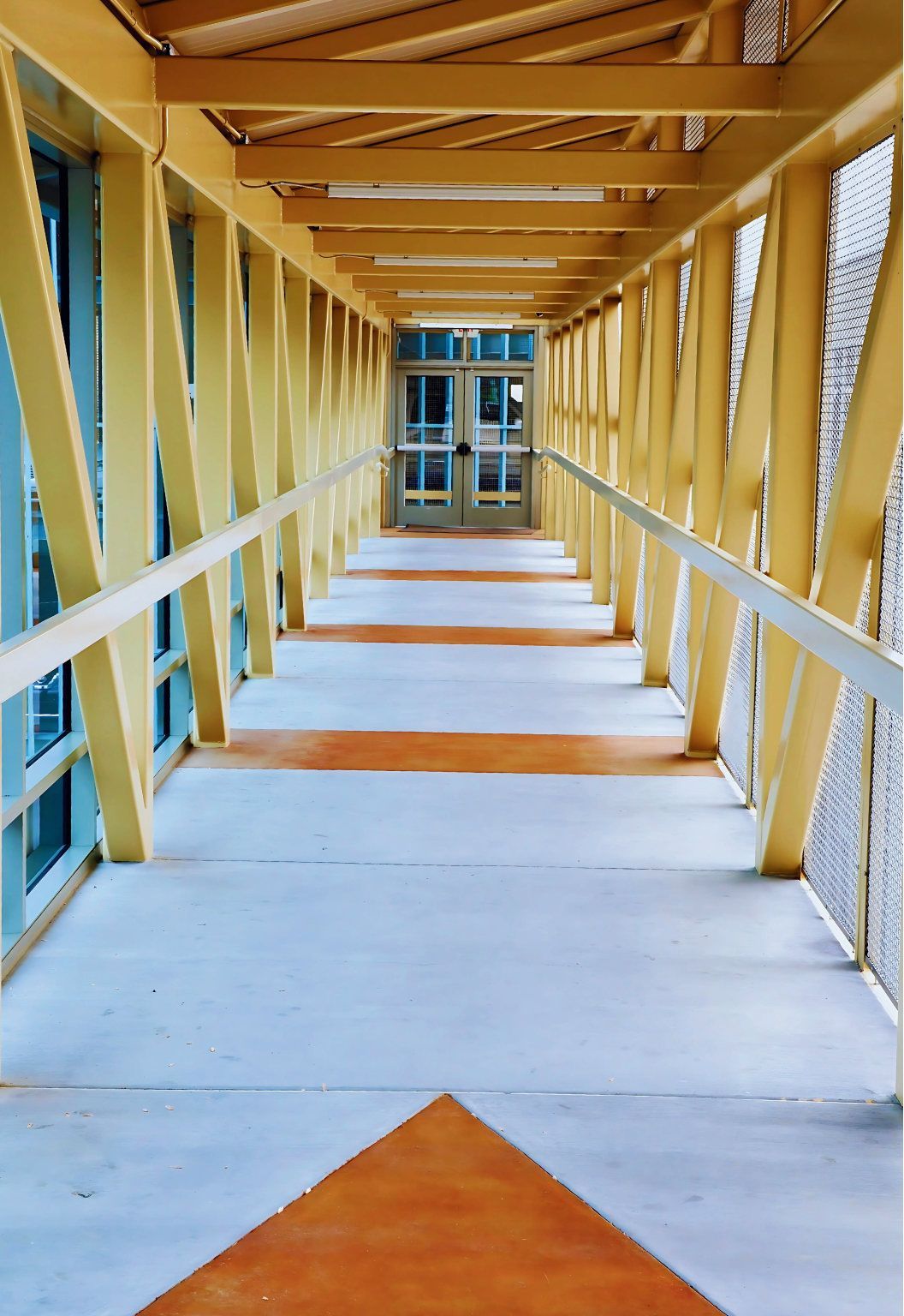 A long hallway with a yellow bridge leading to a building.