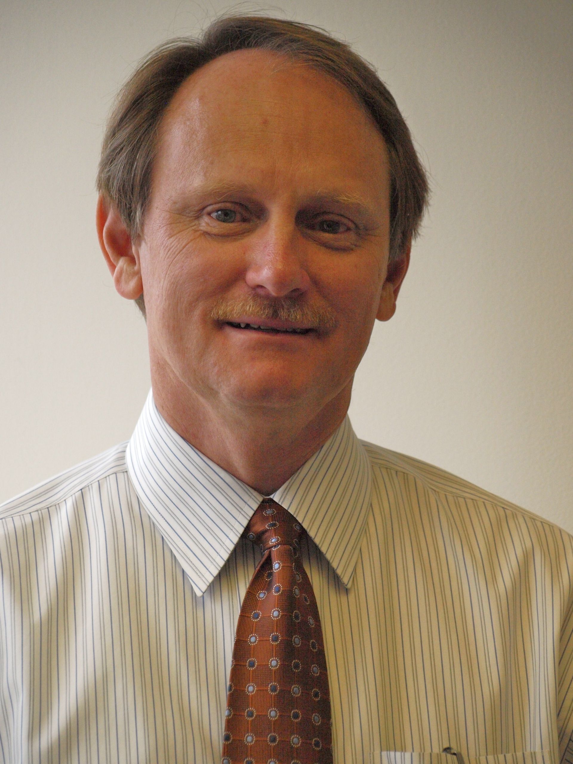 A man wearing a striped shirt and tie is smiling for the camera.