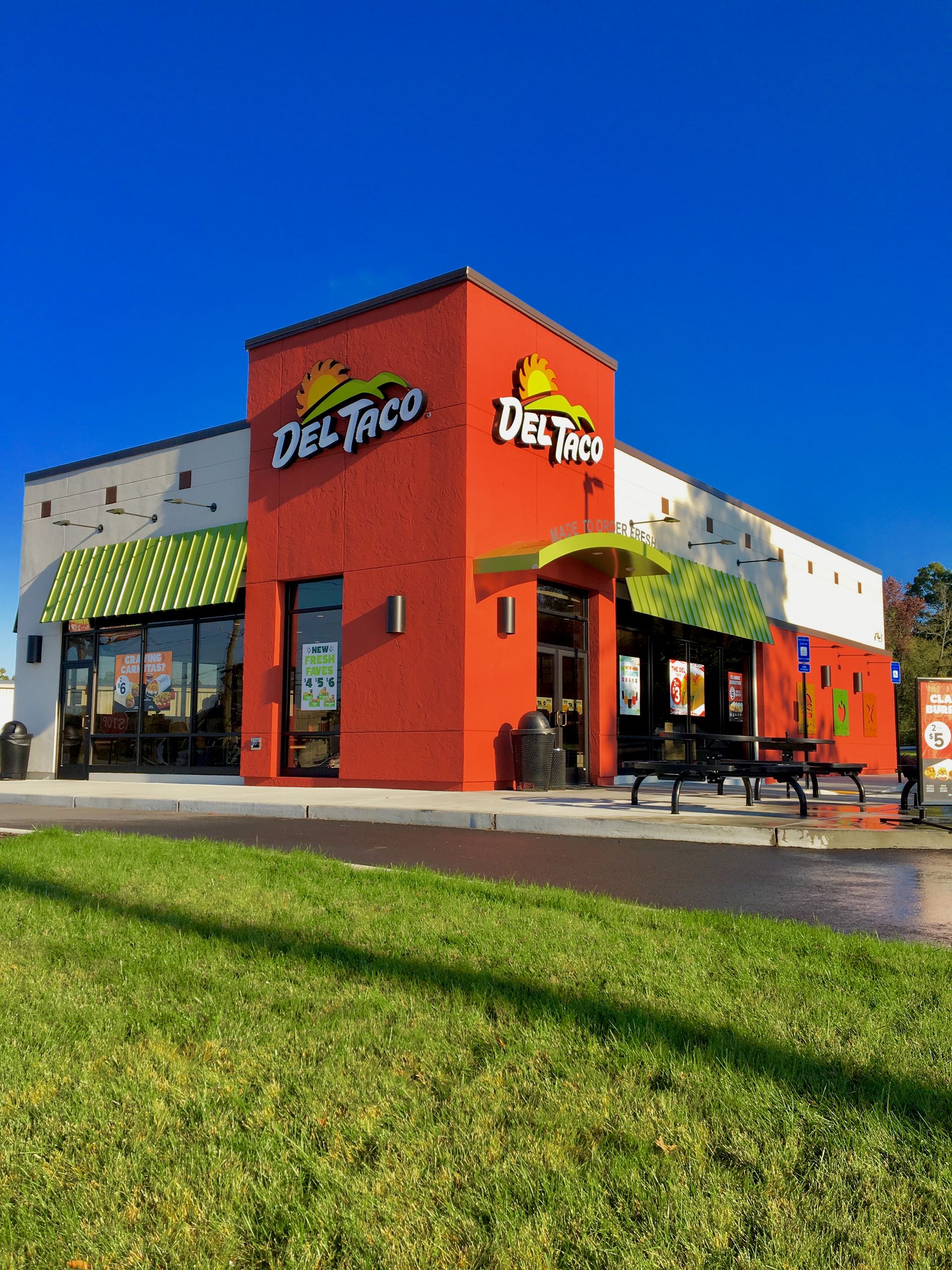 A red and white del taco restaurant with a green awning