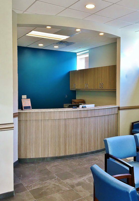 A waiting room with blue chairs and a wooden counter.