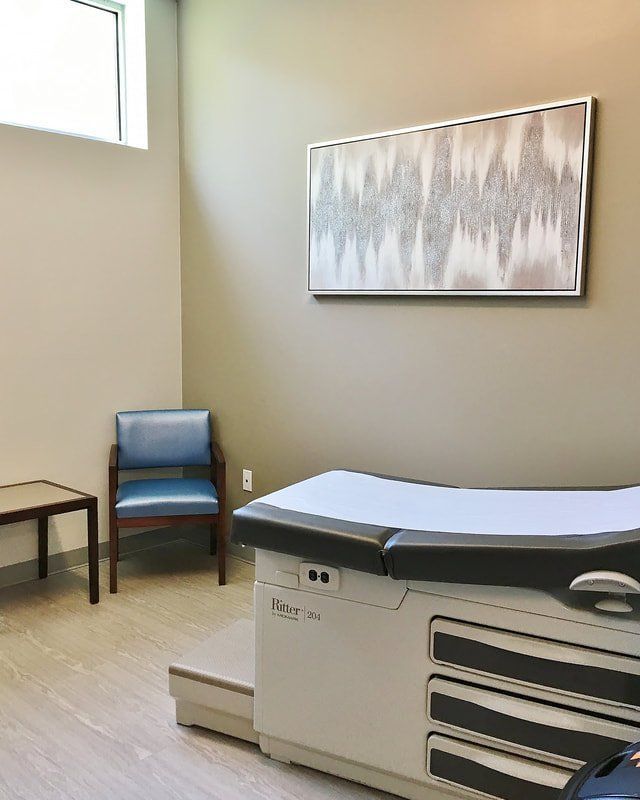 A doctor 's office with a table and chairs and a painting on the wall.