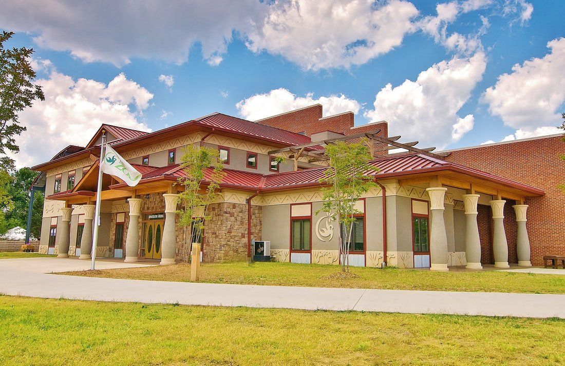 A large building with a red tile roof is surrounded by grass and trees.
